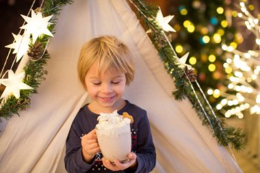 Güzel sarışın çocuk, çocuk, sıcak kakao içiyor. Yanında krema ve Noel süsü var.