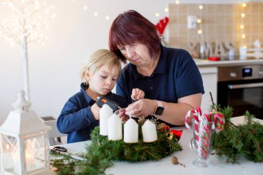 Küçük tatlı sarışın çocuk, oğlum, büyükannesiyle Noel taçlarını süslüyor.