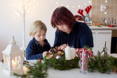 Küçük tatlı sarışın çocuk, oğlum, büyükannesiyle Noel taçlarını süslüyor.