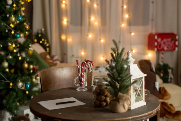 クリスマスの装飾と椅子を備えた古い木製のテーブル テーブルの上に書くために準備された紙 キャンディーの杖とナッツ そして他の部屋の装飾 — ストック写真