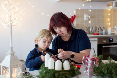 Küçük tatlı sarışın çocuk, oğlum, büyükannesiyle Noel taçlarını süslüyor.