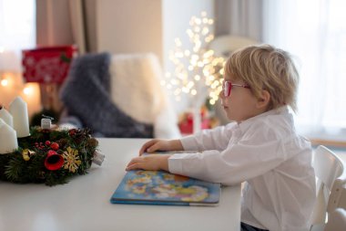 Sıcak Noel atmosferi, çocuk koltukta oturuyor, kitap okuyor, evde Noel bağlarının keyfini çıkarıyor.