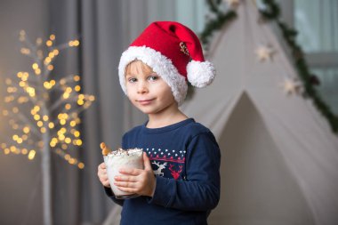 Güzel sarışın çocuk, çocuk, sıcak kakao içiyor. Yanında krema ve Noel süsü var.