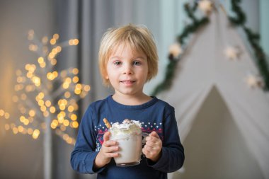 Güzel sarışın çocuk, çocuk, sıcak kakao içiyor. Yanında krema ve Noel süsü var.