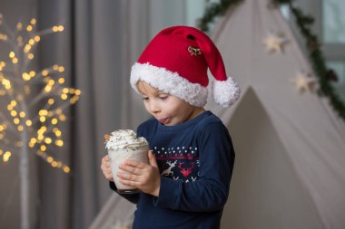Güzel sarışın çocuk, çocuk, sıcak kakao içiyor. Yanında krema ve Noel süsü var.