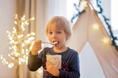 Güzel sarışın çocuk, çocuk, sıcak kakao içiyor. Yanında krema ve Noel süsü var.