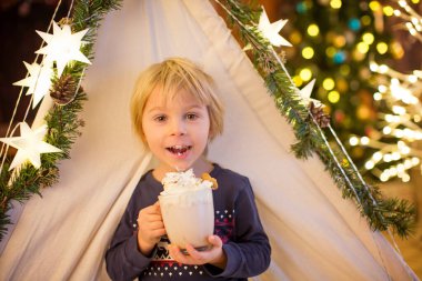 Güzel sarışın çocuk, çocuk, sıcak kakao içiyor. Yanında krema ve Noel süsü var.