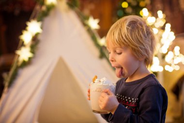 Güzel sarışın çocuk, çocuk, sıcak kakao içiyor. Yanında krema ve Noel süsü var.