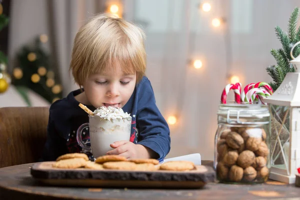 Güzel sarışın çocuk, çocuk, sıcak kakao içiyor. Yanında krema ve Noel süsü var.