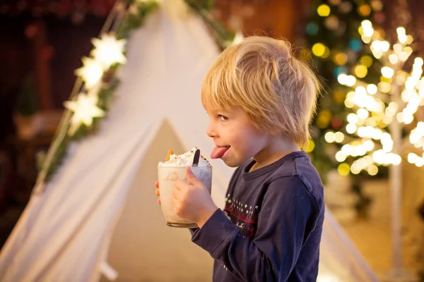 Güzel sarışın çocuk, çocuk, sıcak kakao içiyor. Yanında krema ve Noel süsü var.
