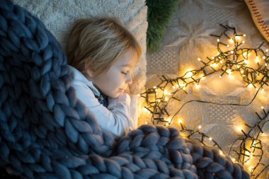Küçük çocuk, tatlı sarışın çocuk, geceleri yatağında Noel ışıklarıyla uyuyor.
