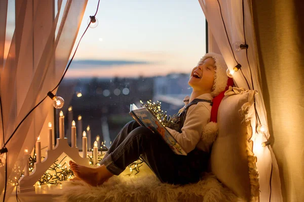 Kleinkind Niedlicher Blonder Junge Sitzt Fenster Liest Buch Weihnachtsbeleuchtung Ihn — Stockfoto