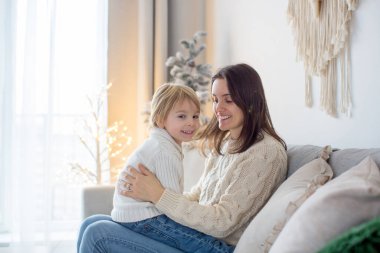 Anne ve çocuk, evde kanepede sarılıyorlar, çocuk annesine sarılıyor, uyuyor ve dinleniyor, ailede birlikte mutluluk var.