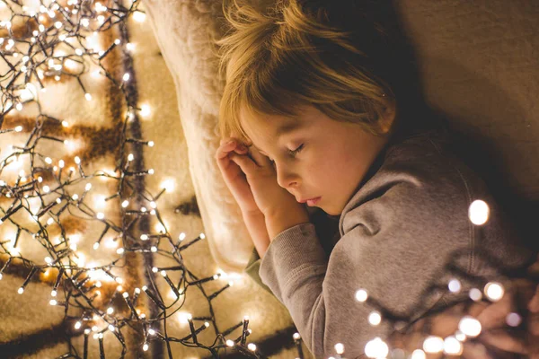 Küçük çocuk, tatlı sarışın çocuk, geceleri yatağında Noel ışıklarıyla uyuyor.