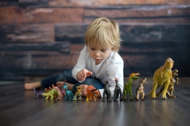 Sarışın küçük çocuk, evde dinozorlarla oynuyor, hoş bir sırt lambası.