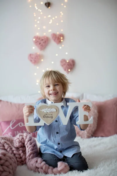 かわいい幼児ブロンドの子供シャツ バレンタインの装飾付きのベッドの上に座って 孤立した背景 — ストック写真