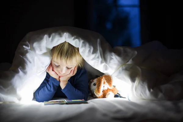 愛らしいブロンド幼児子供 かわいい男の子 読書小さなおもちゃとともに彼の隣にザ Duvetでベッド — ストック写真