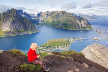Tatlı çocuk, dağların tepesinde oturuyor ve Reinebringen Ağaç Yolu 'na tırmandıktan sonra birçok merdivenle aşağı bakıyor, Lofoten, Kuzey Norveç