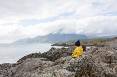 Çocuk, Norveç, Lofoten 'de bir uçurumun kenarından manzaranın keyfini çıkarıyor. İnanılmaz güzel Norveç doğası, yaz zamanı