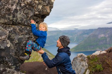Happy child, hanging from a rock over Segla mountain on Senja island, North Norway. Amazing beautiful landscape and splendid nature in scandinavian country