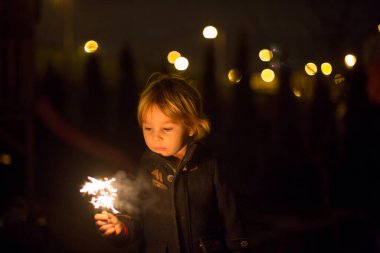 Şirin çocuk, yılbaşı arifesinde elinde maytapla bahçede, mutlu bir çocuk.