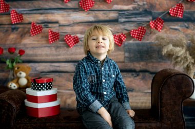 Sevimli sarışın çocuk, sevgililer günü süslemesi, aşkı, çiçekleri olan sevimli çocuk, stüdyoda çerçeveli koltukta oturuyor.