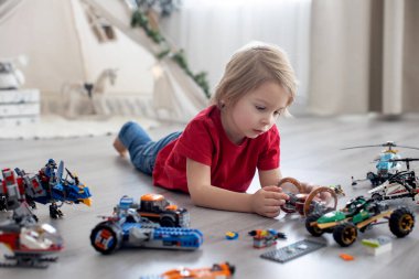 Tatlı çocuk, sarışın çocuk, Colofrul plastik bloklarla oynuyor, inşaat oyuncakları, araba ve uçak yapıyor.