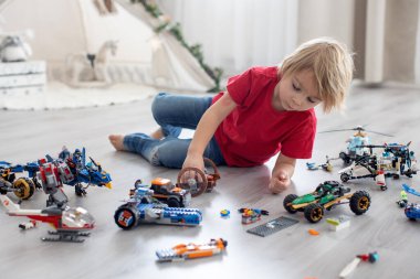 Tatlı çocuk, sarışın çocuk, Colofrul plastik bloklarla oynuyor, inşaat oyuncakları, araba ve uçak yapıyor.