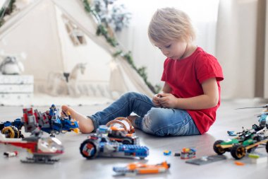 Tatlı çocuk, sarışın çocuk, Colofrul plastik bloklarla oynuyor, inşaat oyuncakları, araba ve uçak yapıyor.