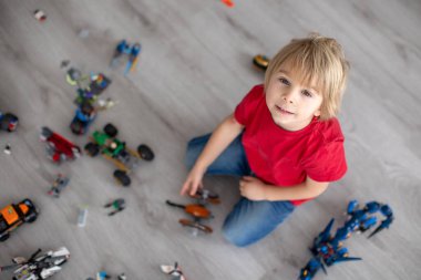 Tatlı çocuk, sarışın çocuk, Colofrul plastik bloklarla oynuyor, inşaat oyuncakları, araba ve uçak yapıyor.