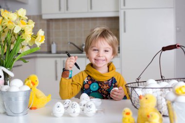 Küçük çocuk, siyah kalemle paskalya yumurtalarına komik ifadeler çiziyor.