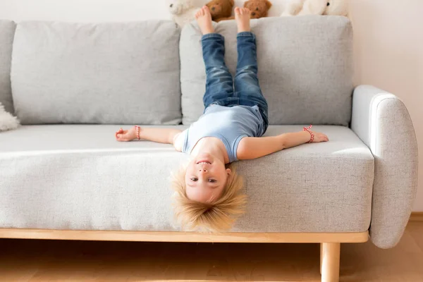 Kisgyerek Fejjel Lefelé Lóg Egy Kanapéról Otthon Boldogan Mosolyog — Stock Fotó