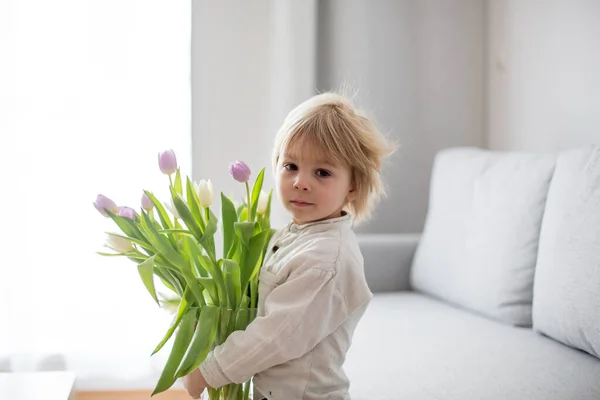 美しいブロンド男の子 与えます母の花とボックスで少しギフトのために母の日に日当たりの良いリビングルーム — ストック写真
