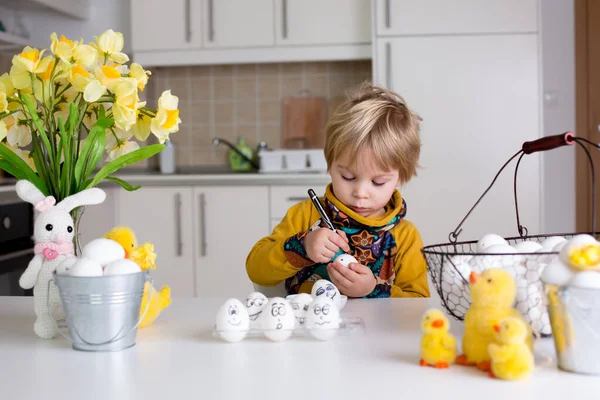 Küçük çocuk, siyah kalemle paskalya yumurtalarına komik ifadeler çiziyor.