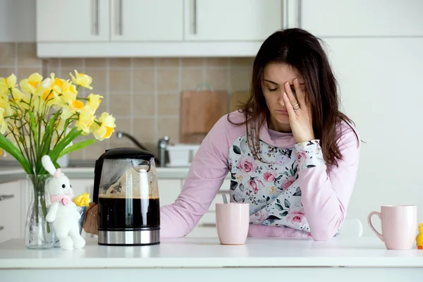 疲れて母親は 午前中にコーヒーを注ぐしようとする 眠れない夜の後台所のテーブルの上に寝そべってコーヒーを飲みに — ストック写真