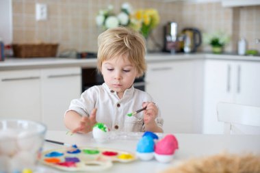 Güzel sarışın çocuk, küçük çocuk, annesiyle evde paskalya yumurtası boyuyor, gökkuşağı renginde Paskalya çelengi yapıyor.