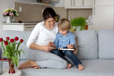 Tatlı çocuk ve annesi, evde kitap okuyor, kanepede oturuyor, dinleniyor, anne evden çalışıyor, ama oğlu için biraz zaman ayırmayı başarıyor.