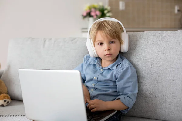 可爱的金发碧眼的孩子 穿着休闲装的男孩 在家操劳计算 带着耳机和电话 — 图库照片