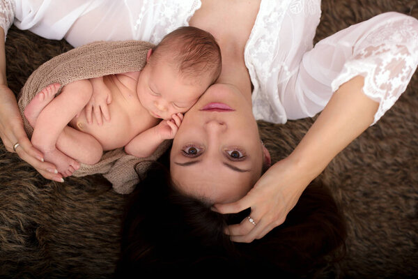 Beautiful mother embracing with tenderness and care her newborn son, shot from above, happiness concept