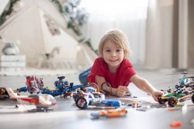 Tatlı çocuk, sarışın çocuk, Colofrul plastik bloklarla oynuyor, inşaat oyuncakları, araba ve uçak yapıyor.