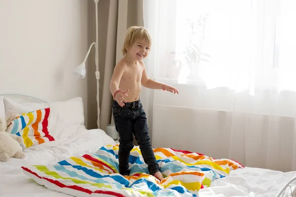 幸せな幼児の子供 カラフルなバスローブを着たブロンドの男の子 ベッドの上でジャンプ 幸せな笑顔 — ストック写真