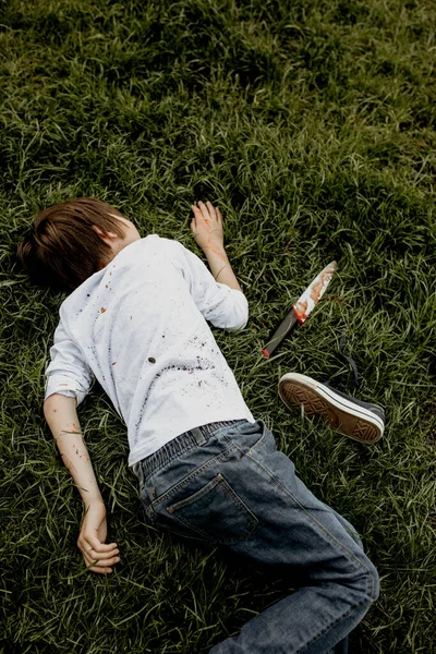 土で覆われた草の上に横たわるティーンエイジャー 彼の隣にナイフ — ストック写真