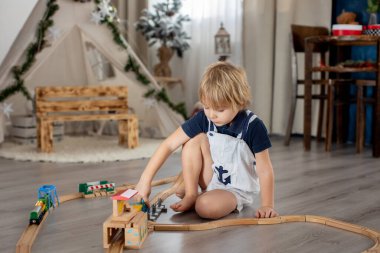 Sevimli sarışın çocuk, evdeki renkli trenlerle ve demiryollarıyla oynuyor.