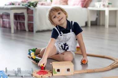 Sevimli sarışın çocuk, evdeki renkli trenlerle ve demiryollarıyla oynuyor.