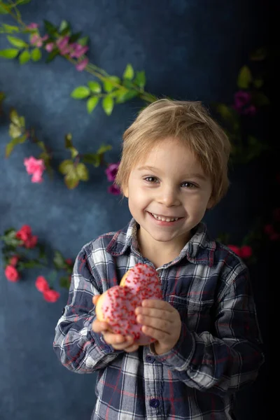 かわいいブロンドの子供 就学前の男の子 ハートの形でピンクのドーナツを食べる バレンタインのために作られた バレンタインの背景 — ストック写真