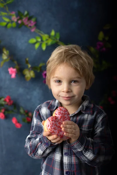 かわいいブロンドの子供 就学前の男の子 ハートの形でピンクのドーナツを食べる バレンタインのために作られた バレンタインの背景 — ストック写真
