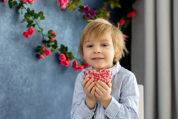 かわいいブロンドの子供 就学前の男の子 ハートの形でピンクのドーナツを食べる バレンタインのために作られた バレンタインの背景 — ストック写真