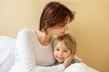Anne ve çocuk, sarışın çocuk, sabahları yatakta sarılıyor, sevgi ve şefkat, aile zamanı.