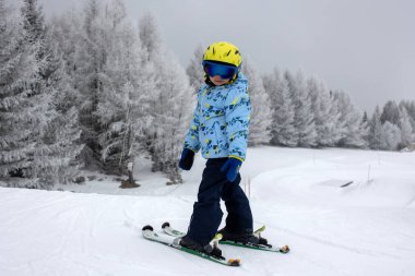 Renkli kayak kıyafetli şirin bir çocuk güneşli bir günde İtalya 'da kayak yapıyor, çocuklar ve yetişkinler birlikte kayak yapıyor. Aile tatili