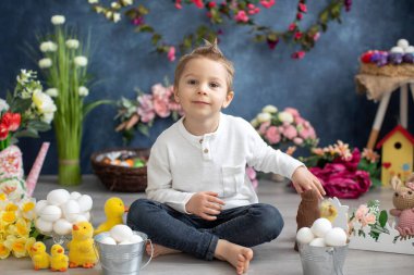 Şirin bir çocuk, beyaz gömlekli bir çocuk, Paskalya süslemesinde yumurta ve çikolatalı tavşanla oynuyor, stüdyo fotoğrafı.